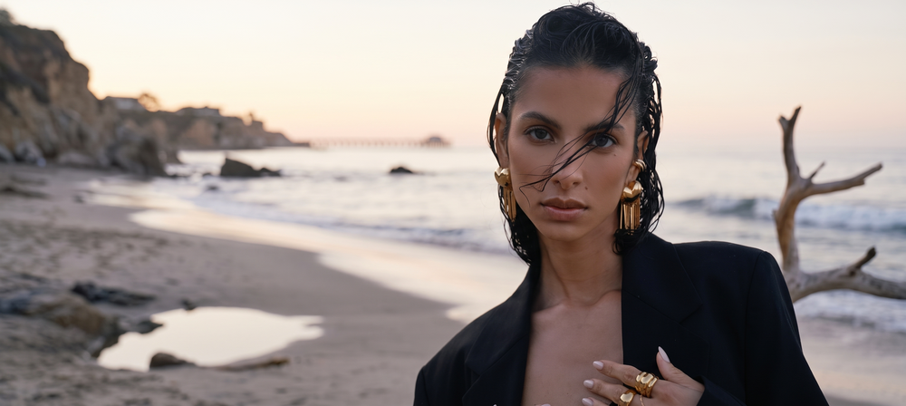 Mujer en la playa al atardecer con pendientes y anillos dorados de Vivante Madrid