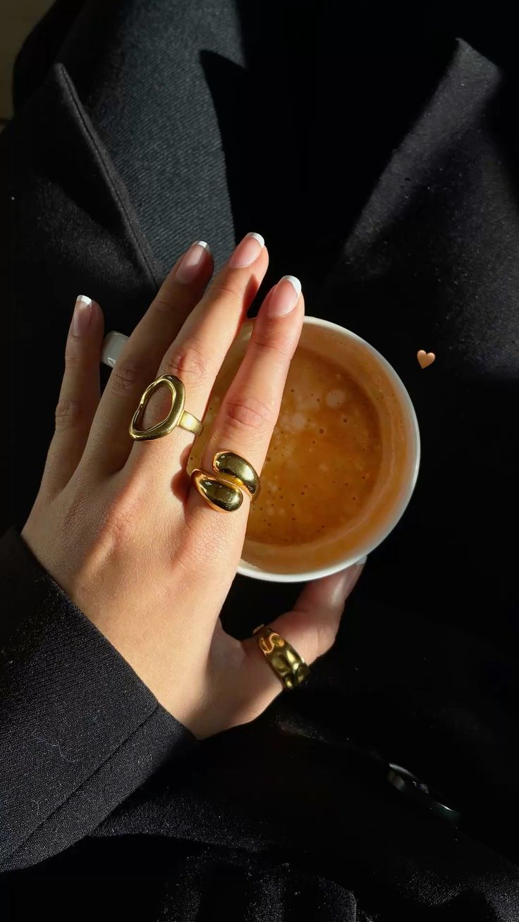 Cliente con anillos dorados escultóricos de Vivante Madrid sujetando un café